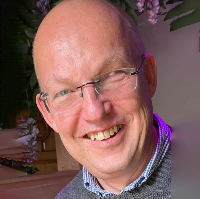 Man wearing glasses is smiling for the camera.