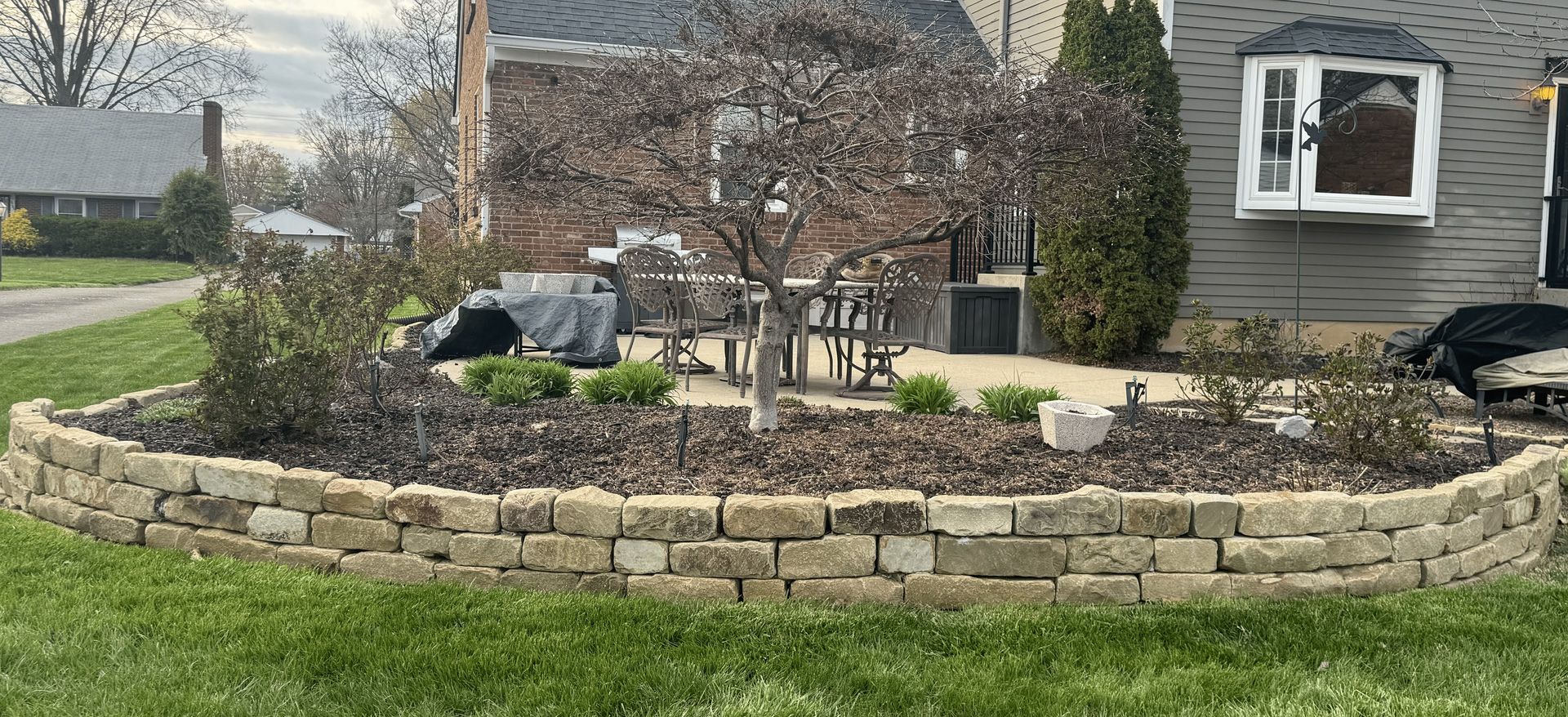 A brick wall surrounds a garden in front of a house.