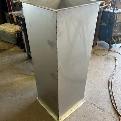 A stainless steel container is sitting on the floor in a workshop.