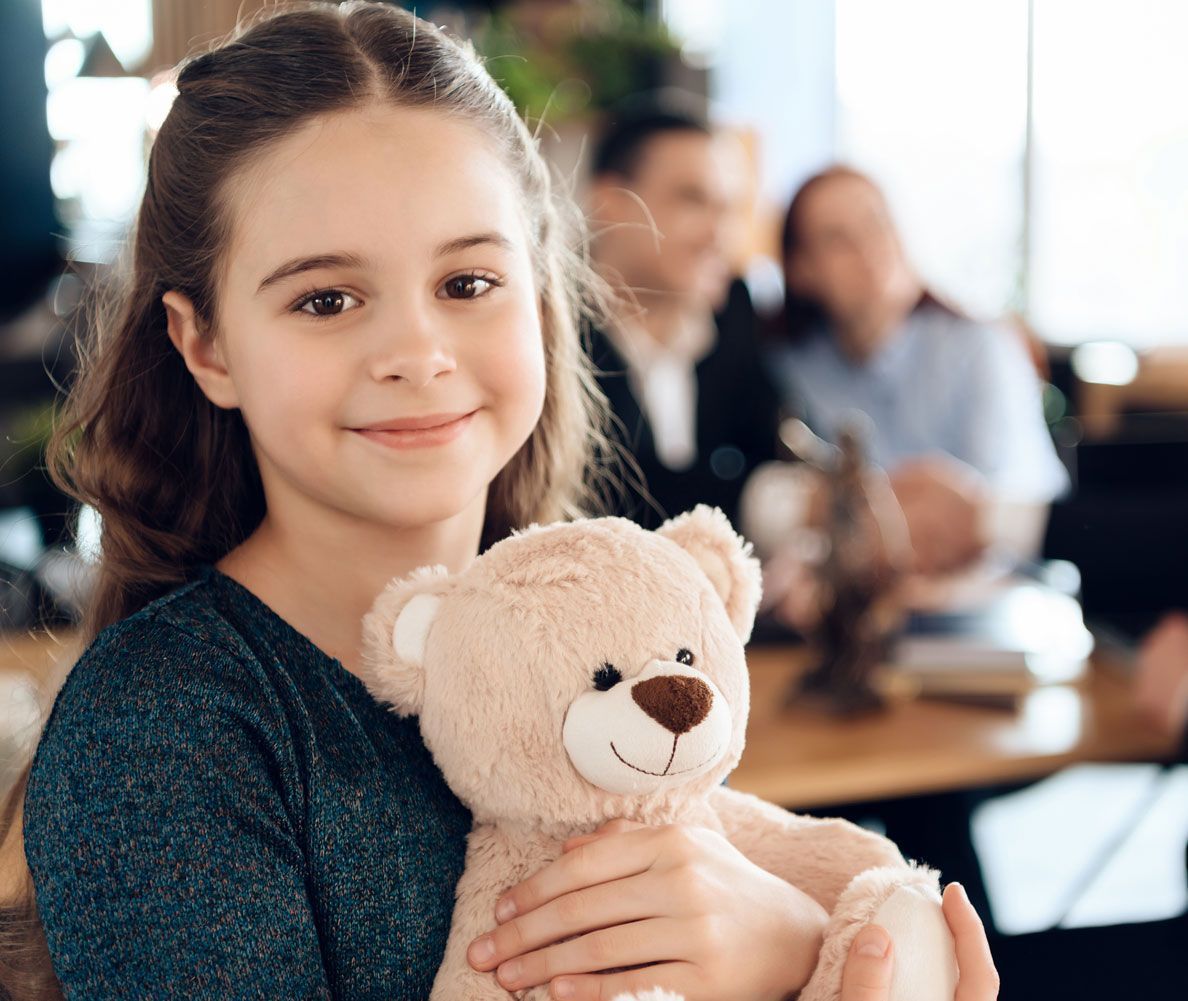 Happy girl hugging teddy bear at office of family lawyer