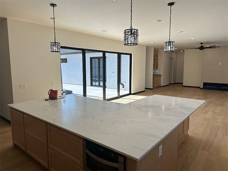 A modern kitchen island with light wood cabinets and white marble countertops sits beneath three industrial pendants.