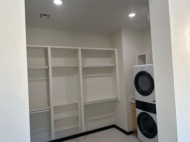 A laundry room with built-in white shelving units next to a stacked washer and dryer.