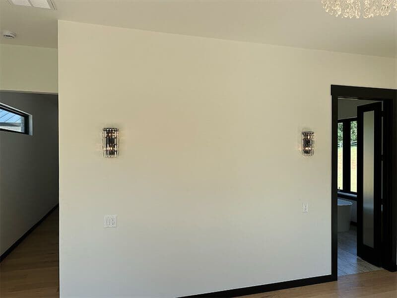An interior wall painted light cream with two matching silver sconces and a door leading to a room with a window.