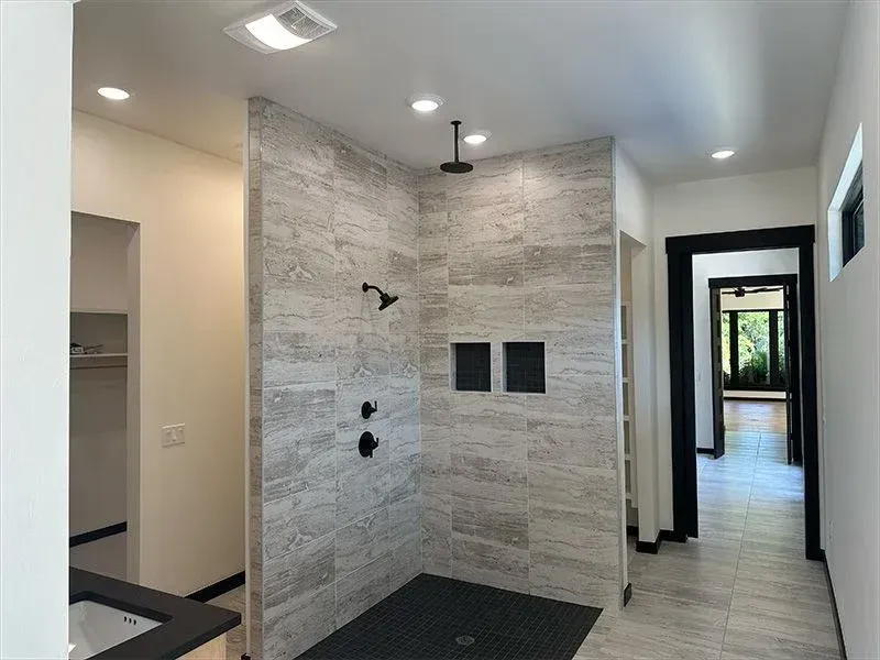 Modern walk-in shower with grey horizontal stone tiles, a black floor, rainfall showerhead, and black hardware.