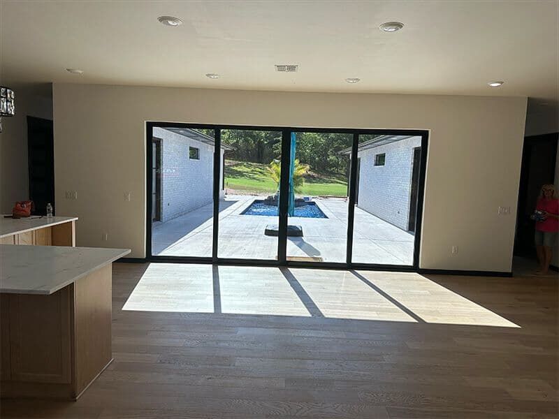 Modern interior room with light wood floors, a kitchen island, and large glass sliding doors overlooking a paved patio.