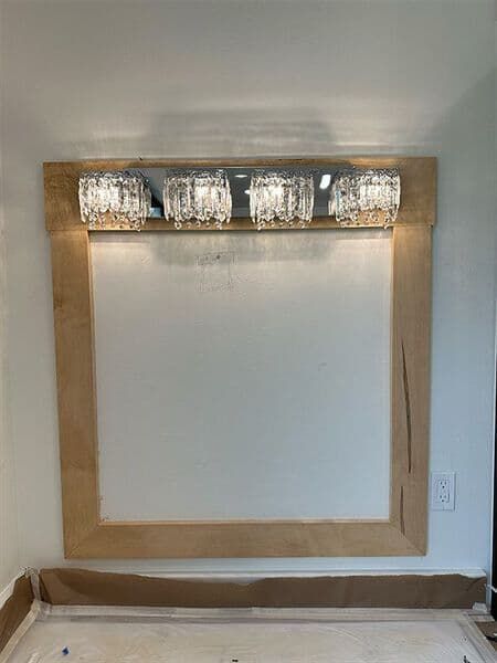A large, rectangular mirror with a light wood frame, topped by a four-bulb chandelier-style light fixture.