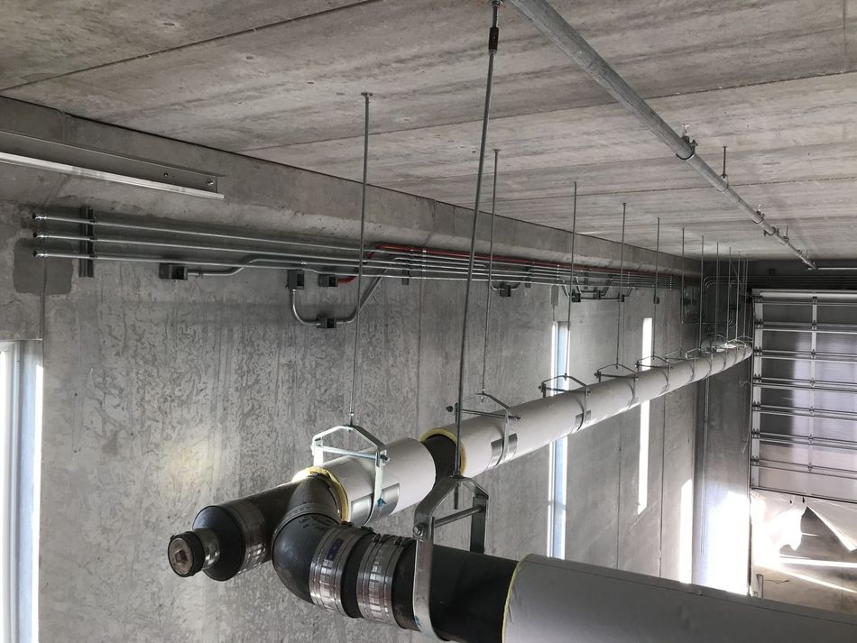 Pipes and electrical conduits suspended from a concrete ceiling in a commercial or industrial space.