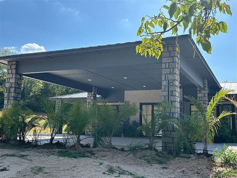 A modern house with a large stone-pillared covered patio, dark gray ceiling with recessed lights, and surrounding plants.