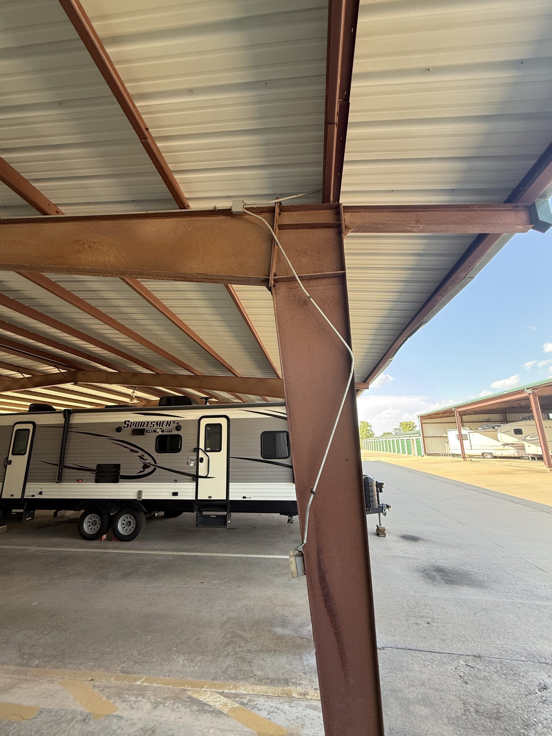 A bent, rusted metal support beam for a covered RV parking structure, with a thin wire wrapped around it.