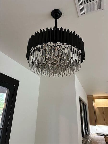 A round chandelier with a black pleated drum shade and hanging clear crystal accents suspended from a white ceiling.