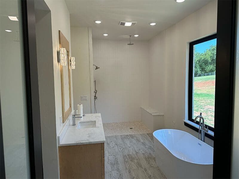 Modern bathroom with a wooden vanity, a freestanding white tub by a window, and a walk-in shower with light tile flooring.