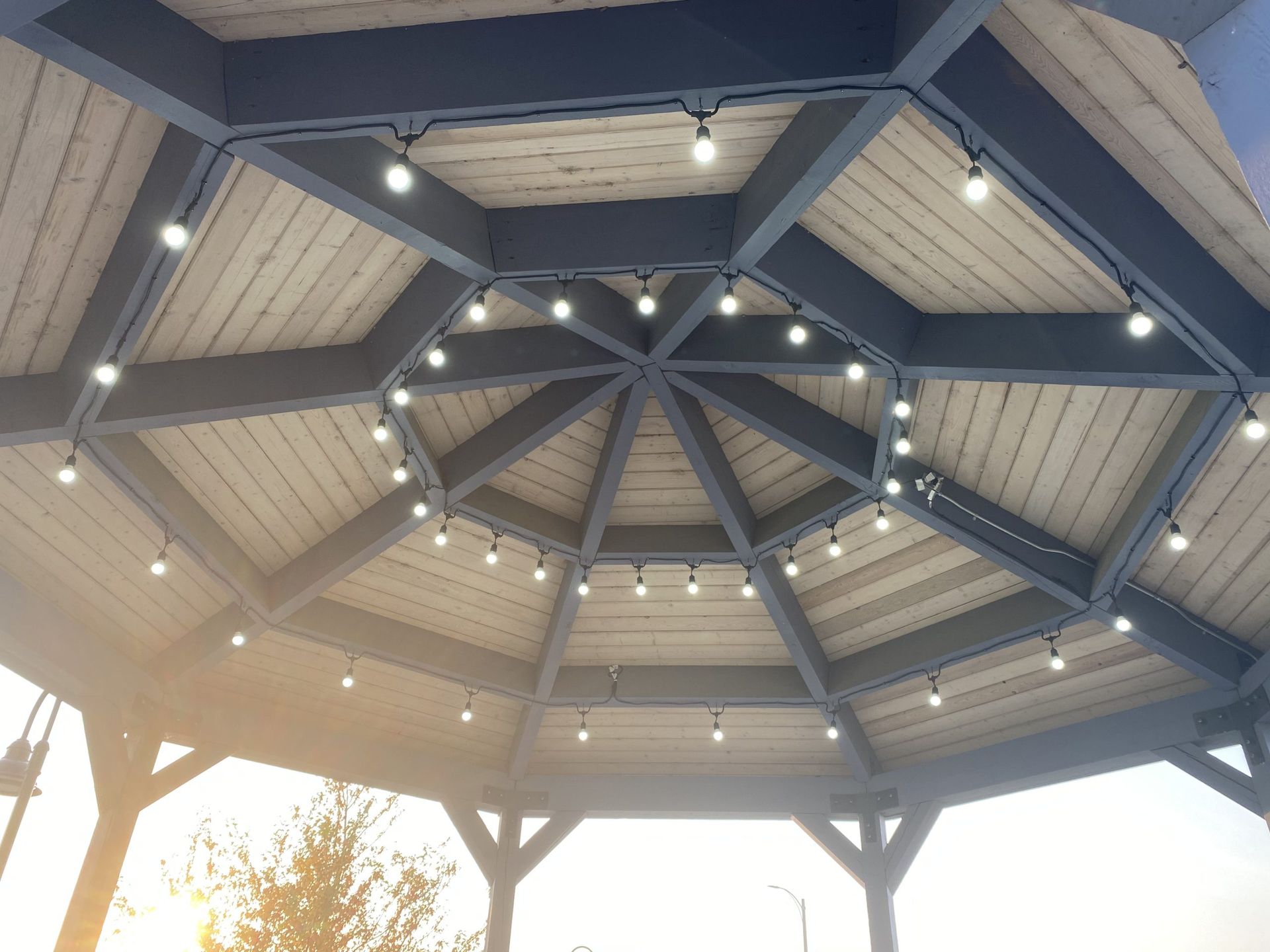 Low-angle view of a grey wooden gazebo ceiling with two concentric rings of glowing string lights.
