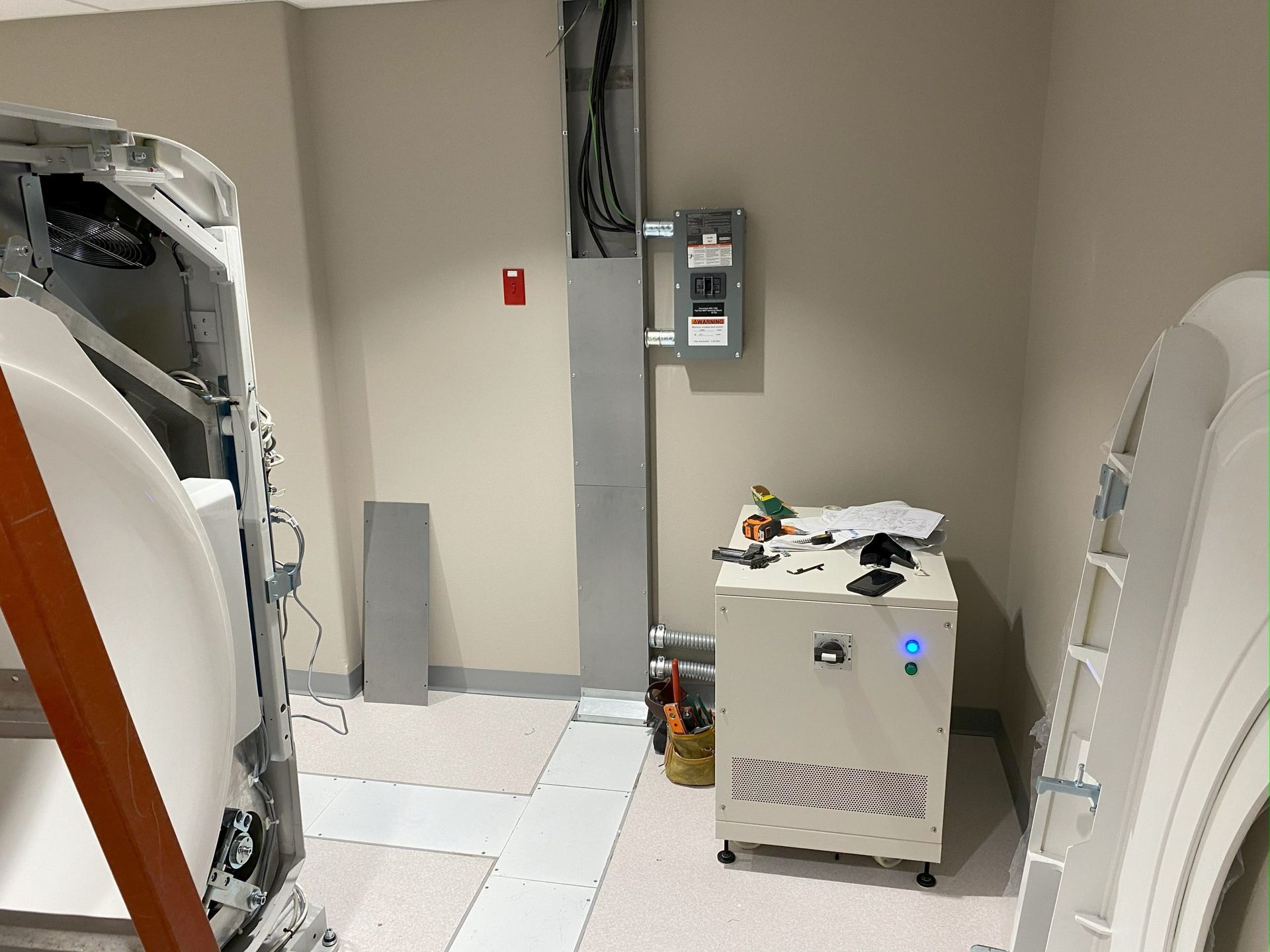 An interior view of a medical room with a CT scanner, electrical panels, and equipment on the floor.