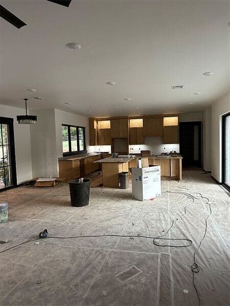 A construction-phase kitchen with light wood cabinets, an island, and floor protection paper covering the floor.