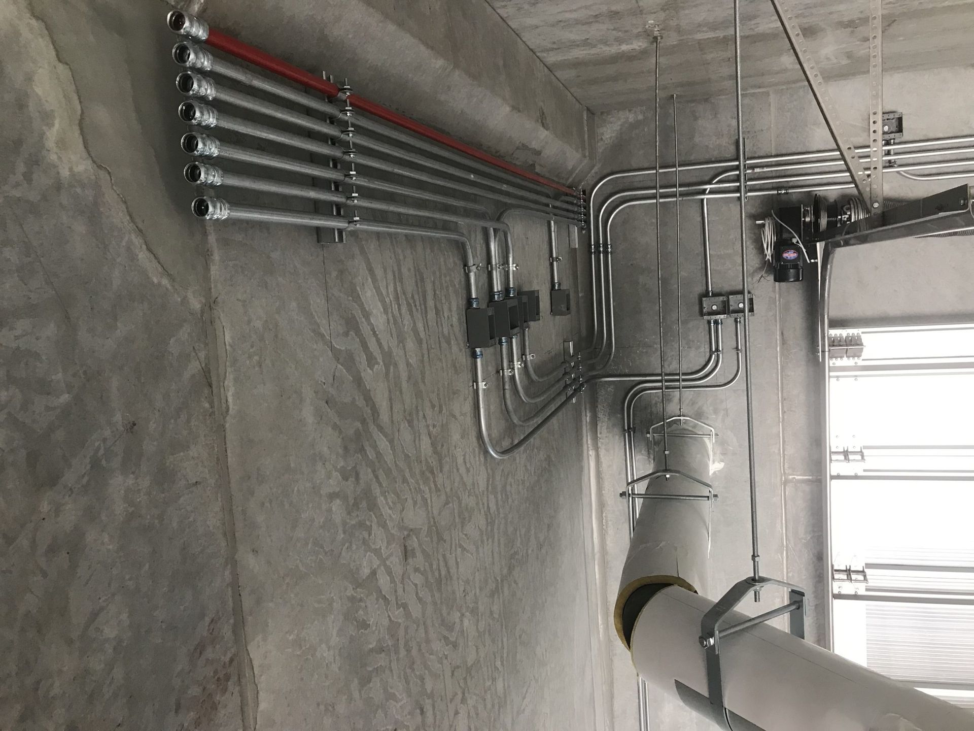 Exposed electrical conduit piping running along a concrete wall and ceiling in a construction site.