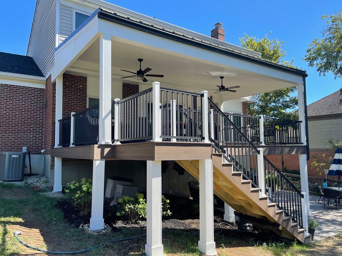 A large deck with stairs leading up to it is in the backyard of a house.