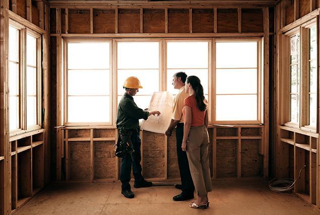 A man and a woman are looking at a blueprint in a room under construction.