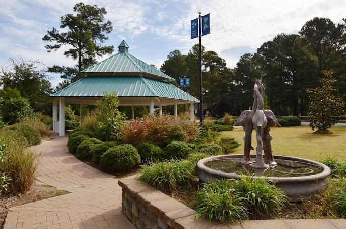 Park gazebo with teal roof beside a fountain and landscaped garden path.