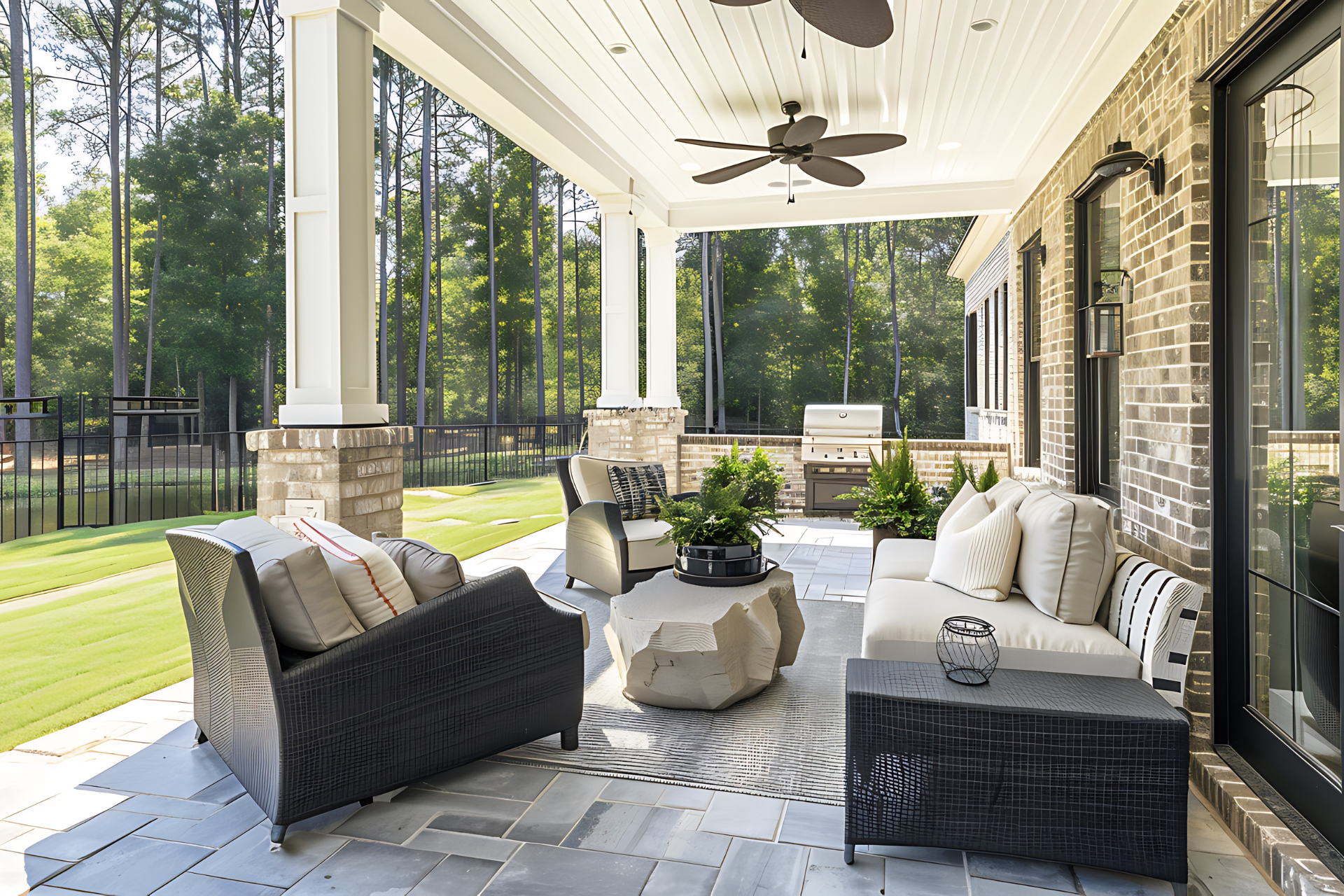 Covered patio with seating, stone table, and grill, overlooking a green lawn and trees.