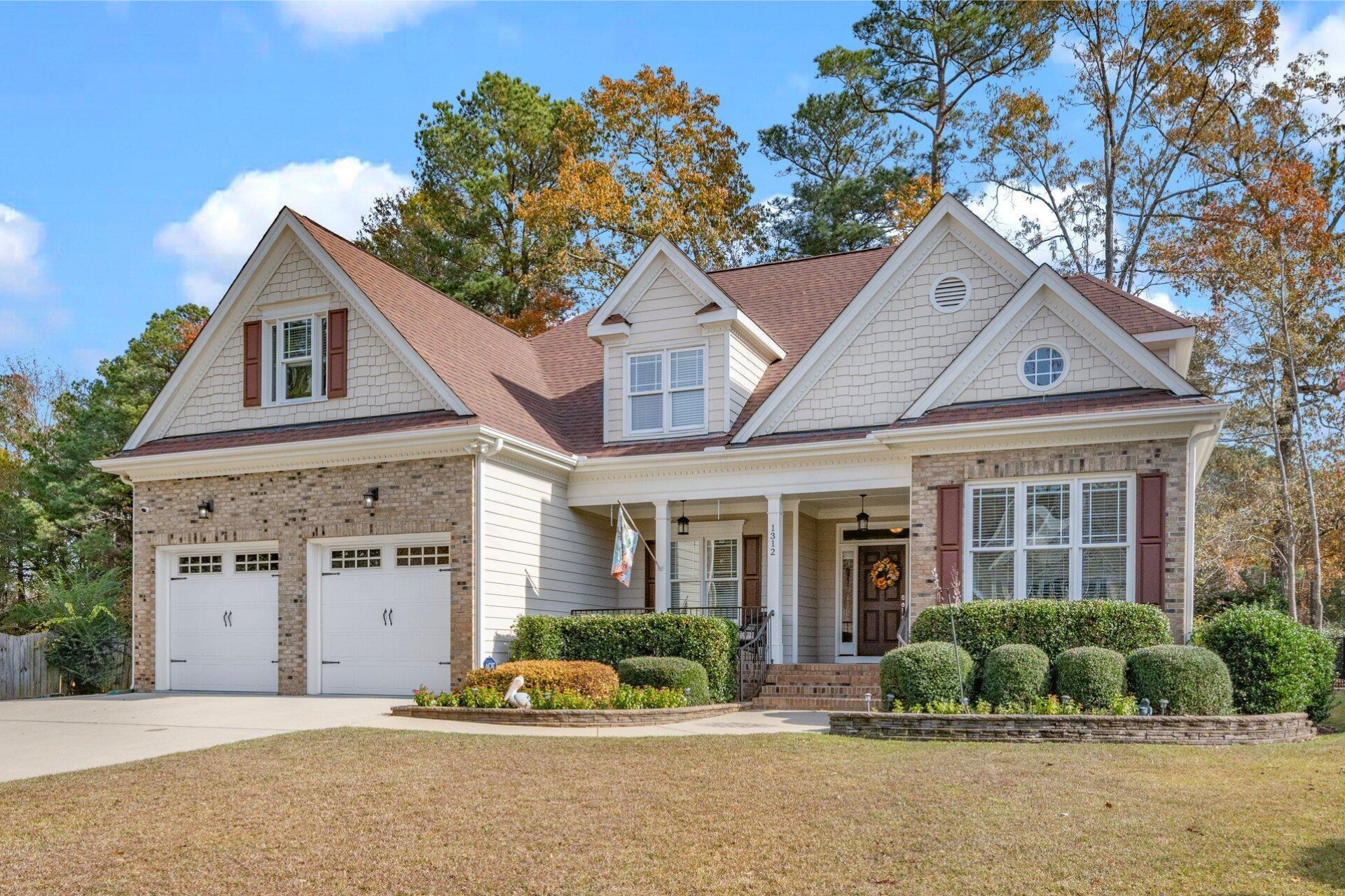 Two-story brick house with beige siding, brown roof, and front lawn.