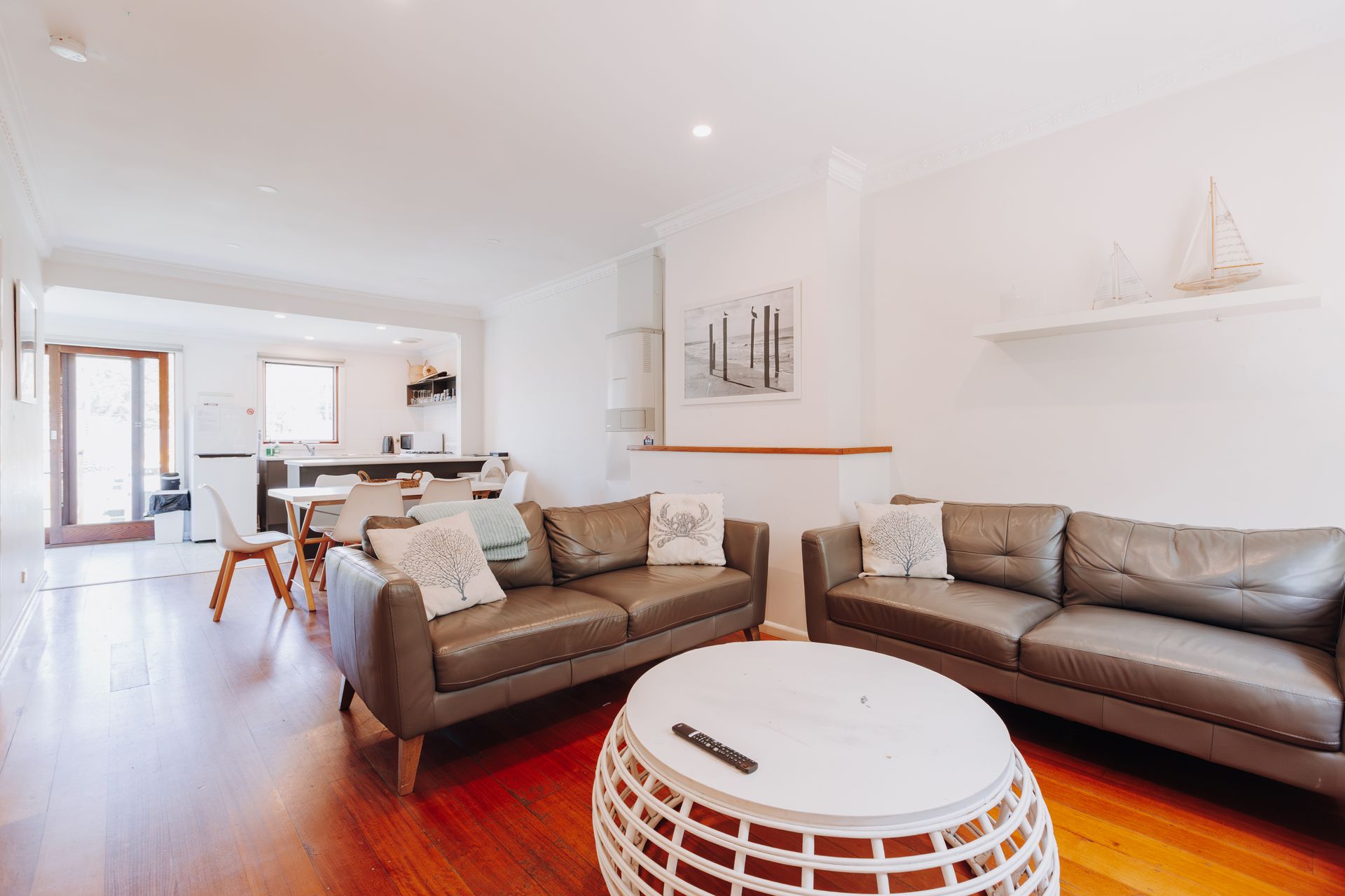 A living room with two brown leather couches, a white circular coffee table, and a kitchen area in the background.