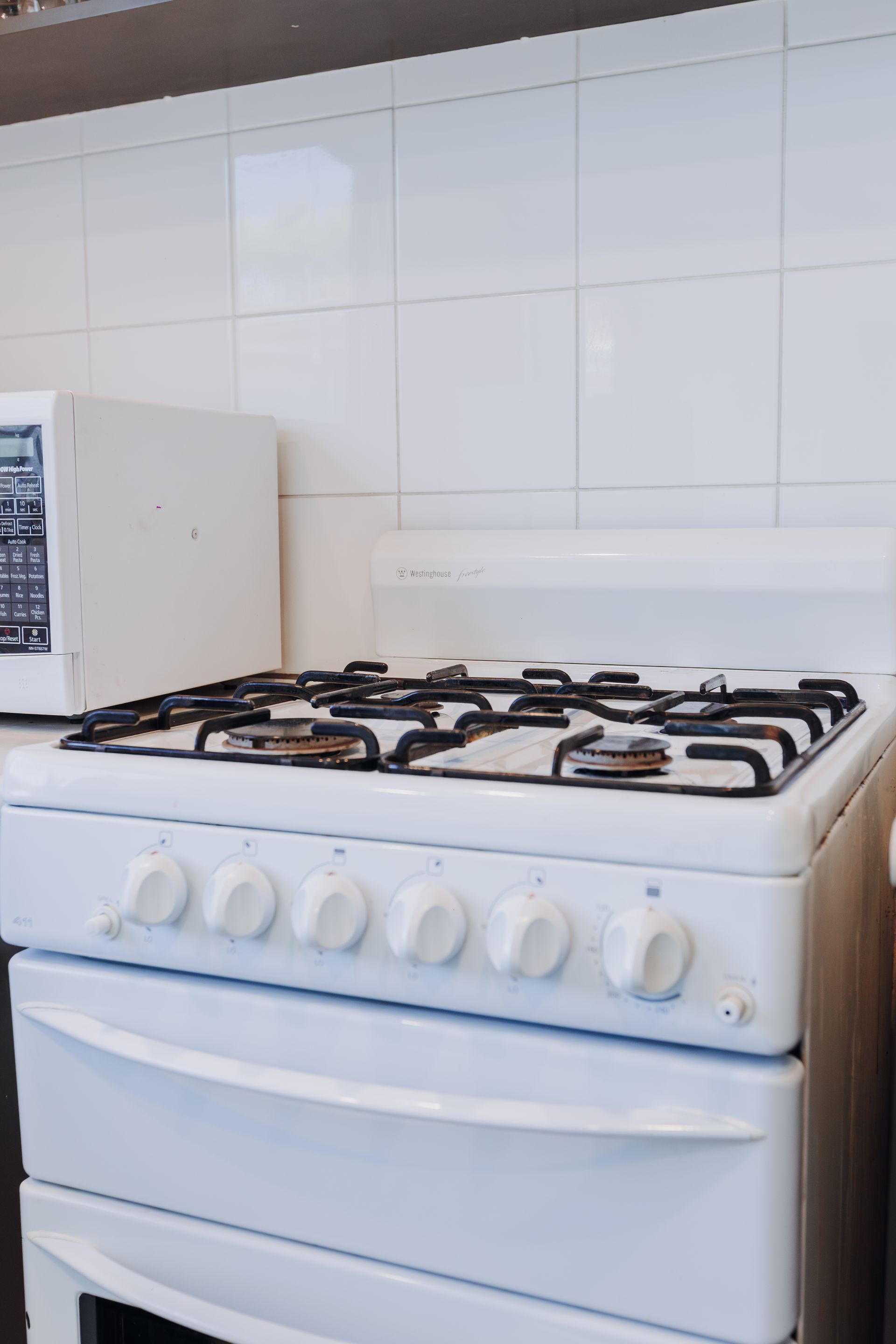 A white gas stove sits in a kitchen with a white tiled backsplash, next to a matching white microwave.
