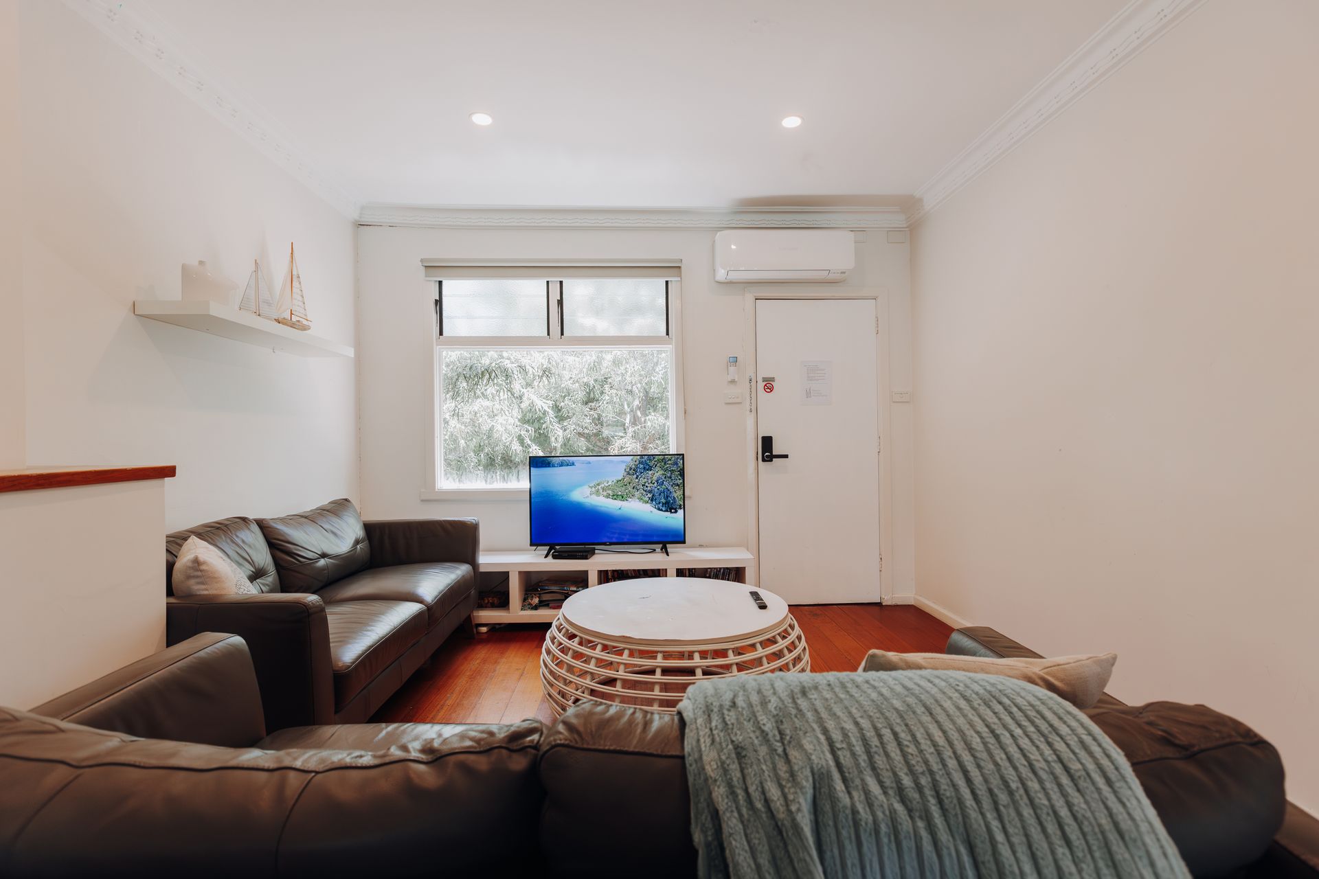 A living room with two dark leather sofas, a central round coffee table, a TV, and a white door in a bright, modern space.