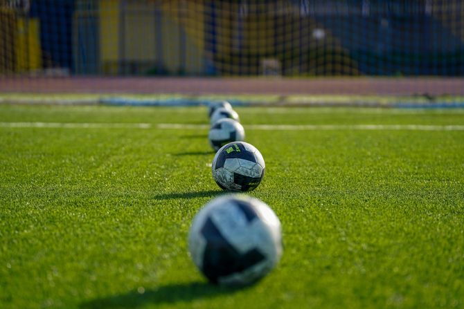 Soccer balls lined up on green turf with a blurred goal in the background
