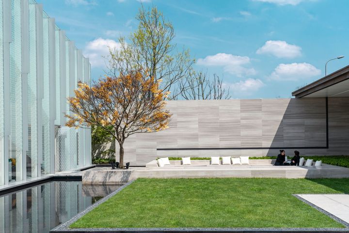 Modern courtyard with green lawn, tree, bench seating, and glass building under a blue sky