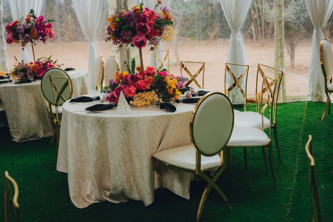 Elegant outdoor event table with white chairs, colorful floral centerpieces, and sheer draped canopy accents
