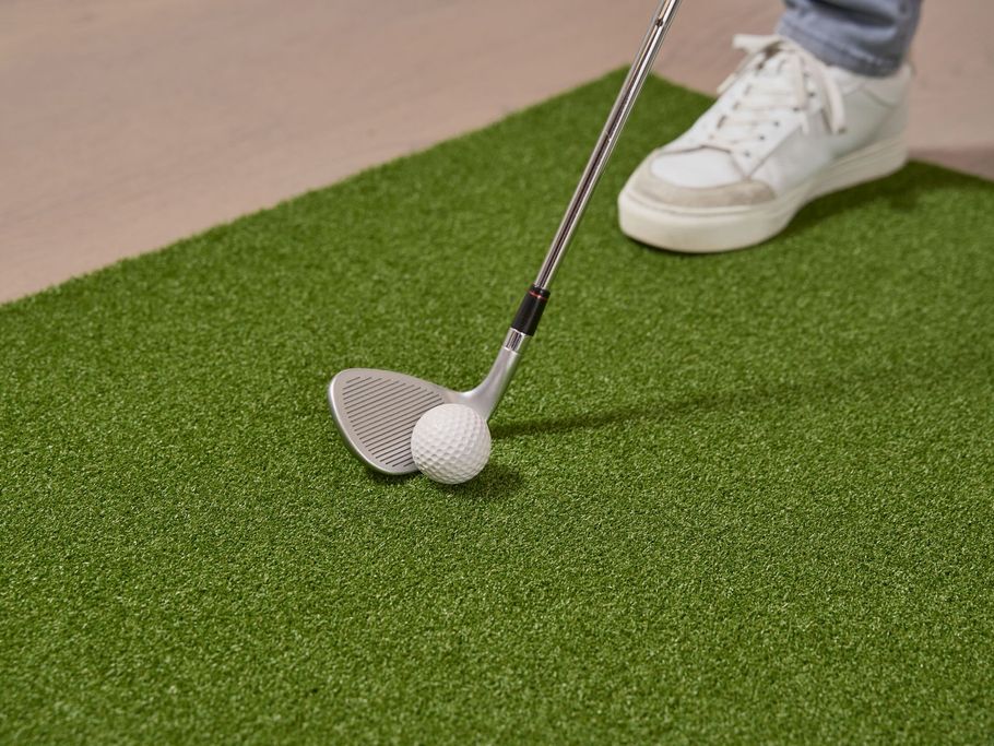 Golfer putting a white ball on green turf near a club head and white shoe