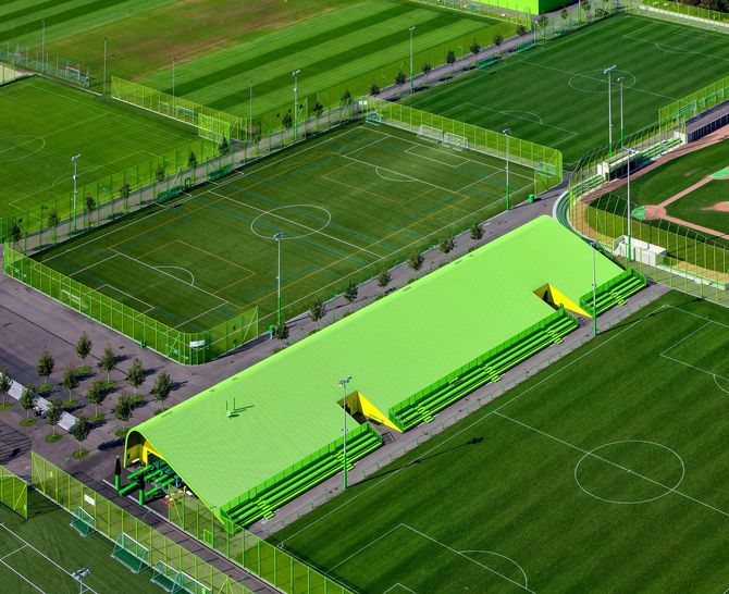 Aerial view of a soccer complex with several green fields and a bright lime-green covered stand.