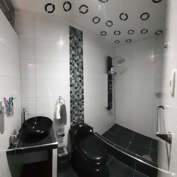 Baño compacto en blanco y negro con lavabo, inodoro, ducha y luces de techo circulares.