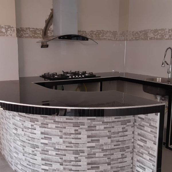 Cocina moderna con encimera negra, placa de gas, frontal curvo alicatado y campana extractora mural.