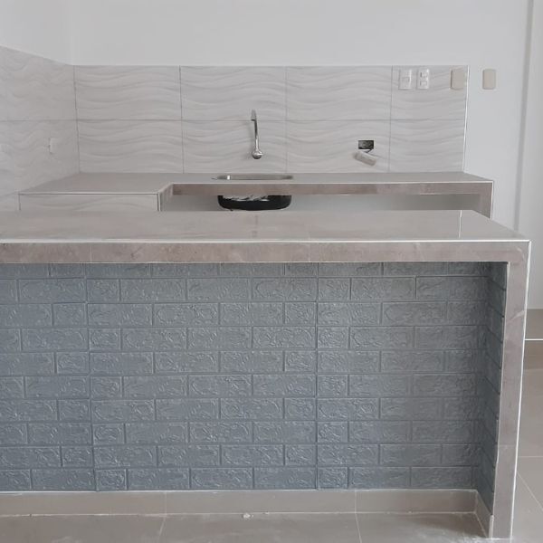 Cocina moderna con isla de azulejos grises, fregadero y salpicadero blanco.
