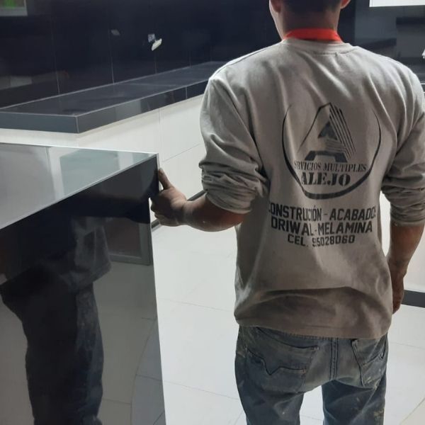 Un trabajador con camisa gris y vaqueros está de pie junto a un mostrador en un espacio interior moderno.