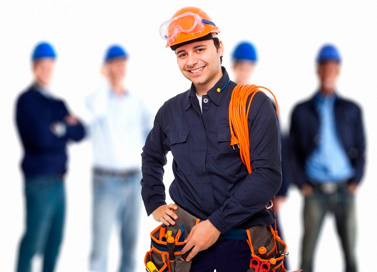 Un obrero de la construcción, con casco naranja y chaleco de seguridad, se encuentra de pie frente a sus compañeros de trabajo, cuyas imágenes se ven borrosas.