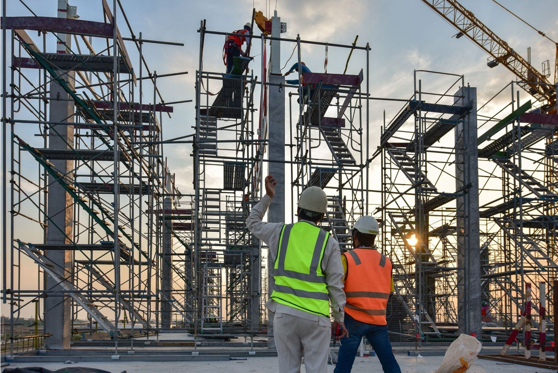 Obreros de la construcción con chalecos de seguridad en andamios en una obra, inspeccionando la estructura de acero.