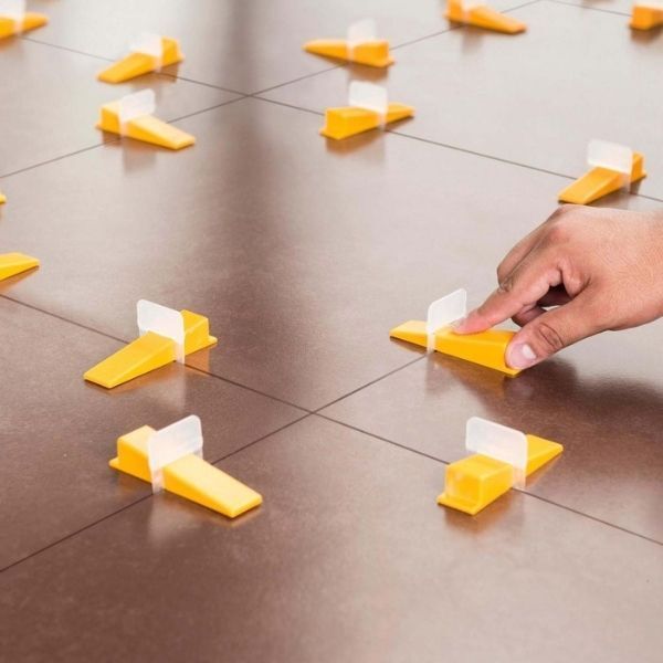 Una mano coloca un avión de papel amarillo y blanco entre varios sobre un suelo de baldosas.