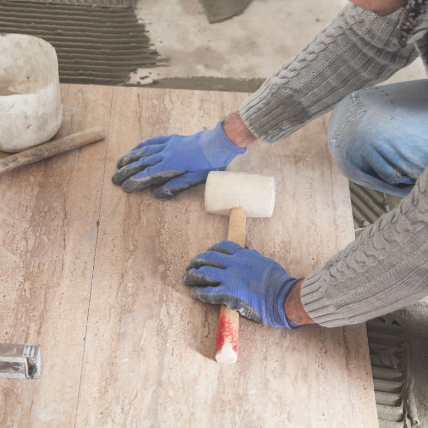 Persona con guantes aplicando material con una llana sobre una tabla de madera en una obra de construcción.