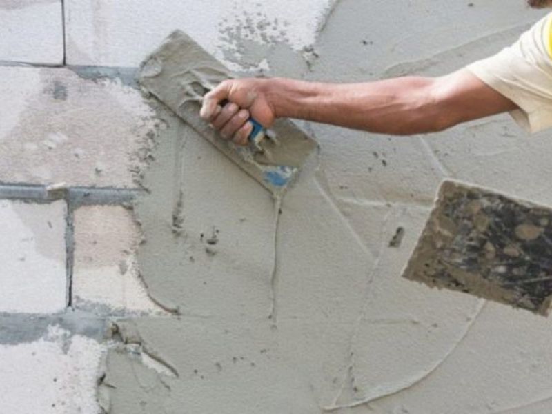 Alisar a mano el yeso de una pared dañada con una llana.