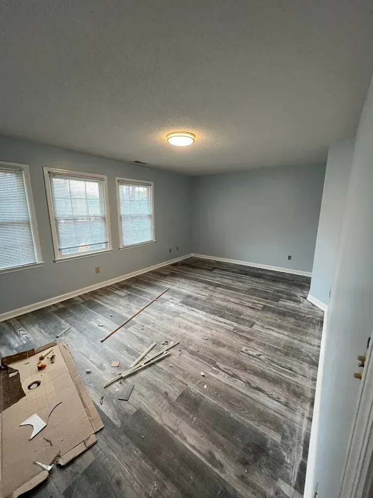 Empty room with gray walls, hardwood floor being installed, and three windows letting in daylight
