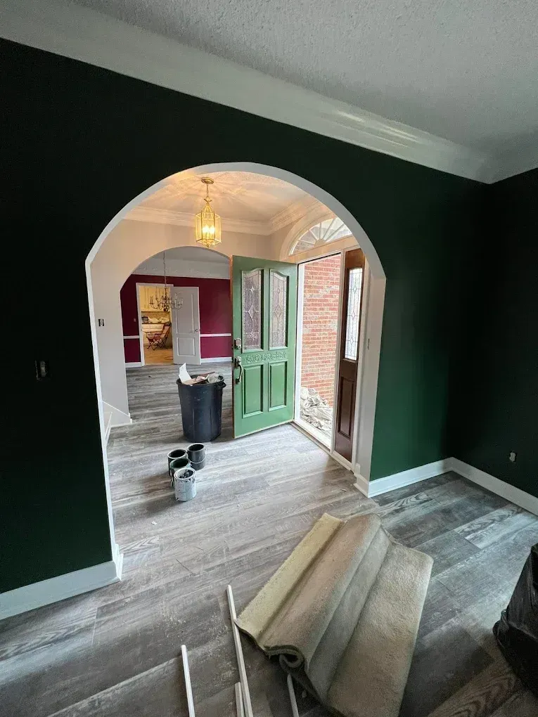 Empty living room with dark green walls, archway to a kitchen, and rolled carpet on the floor.