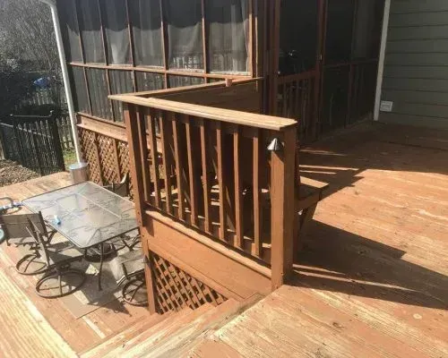 Wooden porch deck with railing and steps beside a small patio table and chairs in sunlight