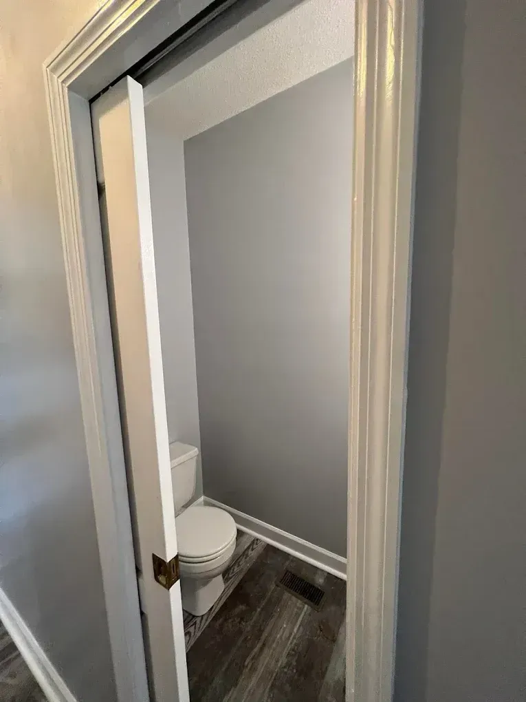 Small bathroom with an open door, showing a toilet and gray walls inside.