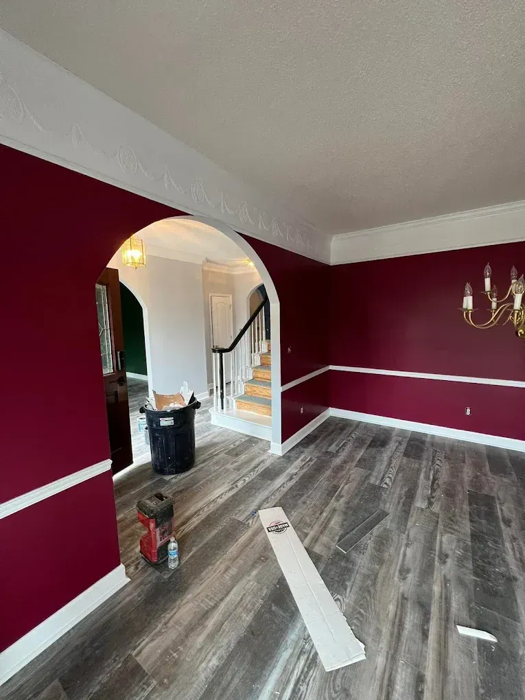 Empty living room with burgundy walls, gray floor, arched doorway, and chandelier lighting.