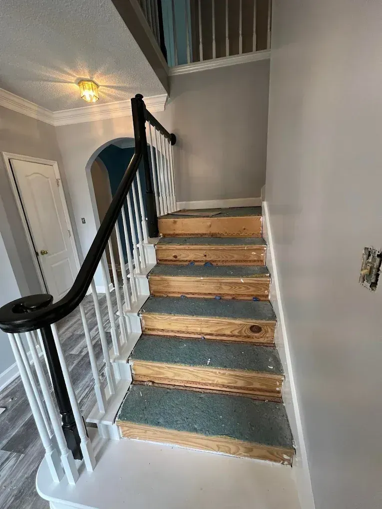Interior staircase with wooden steps, blue carpet runners, white railing, and gray walls.