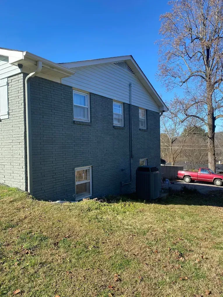 Side view of a gray house with white trim, grassy yard, and a red car parked nearby.