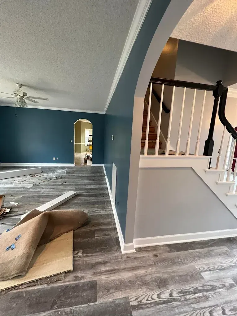 Living room with gray wood floors, teal walls, arched opening, and staircase with black railing