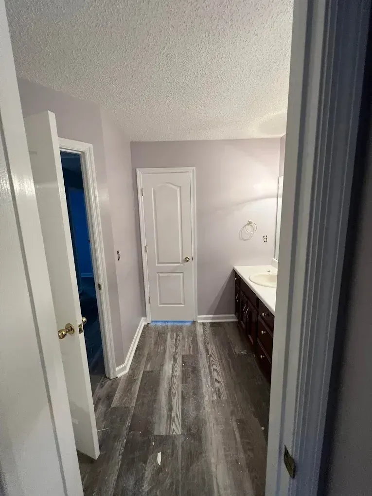 Narrow bathroom hallway with gray flooring, white door, and dark vanity beside a sink.